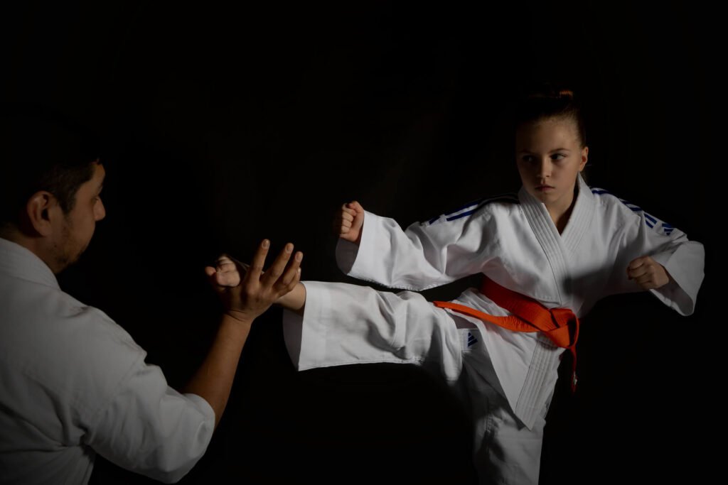 Kouluikäinen tyttö harjoittelee potkutekniikkaa taistelulajien opettajan kanssa